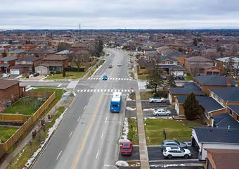 Intersection on Martin Grove Road featuring pedestrian crosswalks, cars, buses and nearby homes. 