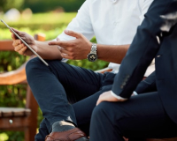 two people in business attire sitting on a bench consulting a clipboard