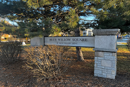Entrance to Blue Willow Square, sign with park name and address, trees, shrubs and grass