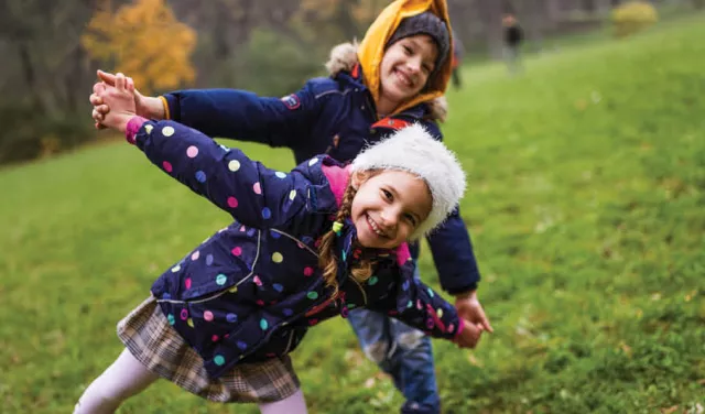 2 children playing outdoors wearing a colourful jacket