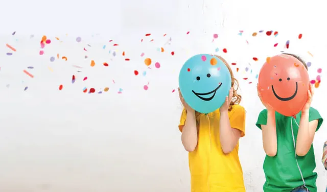 Line of kids with colourful balloons with smiley faces on them 