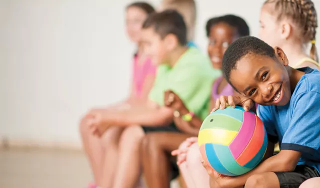 young boy holding a volleyball while sitting on the bench with his friends