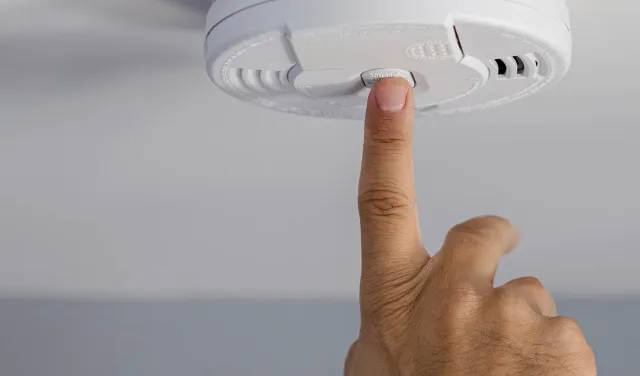Finger pressing button on ceiling smoke detector