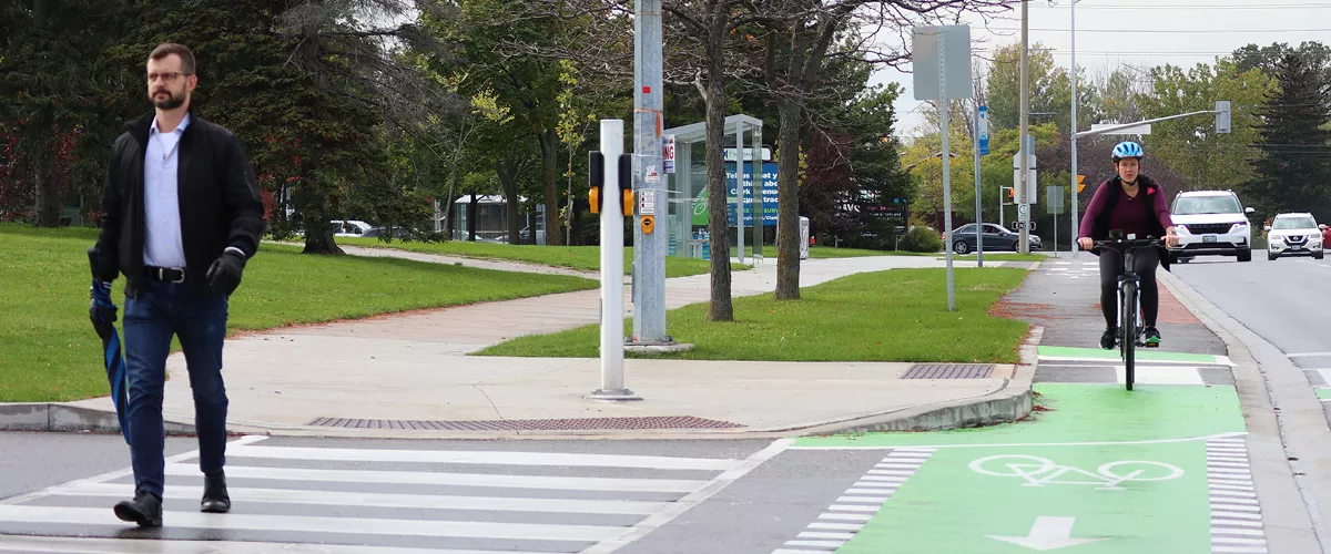 A person walking across a pedestrian crosswalk and a cyclist riding in a designate bike-lane.