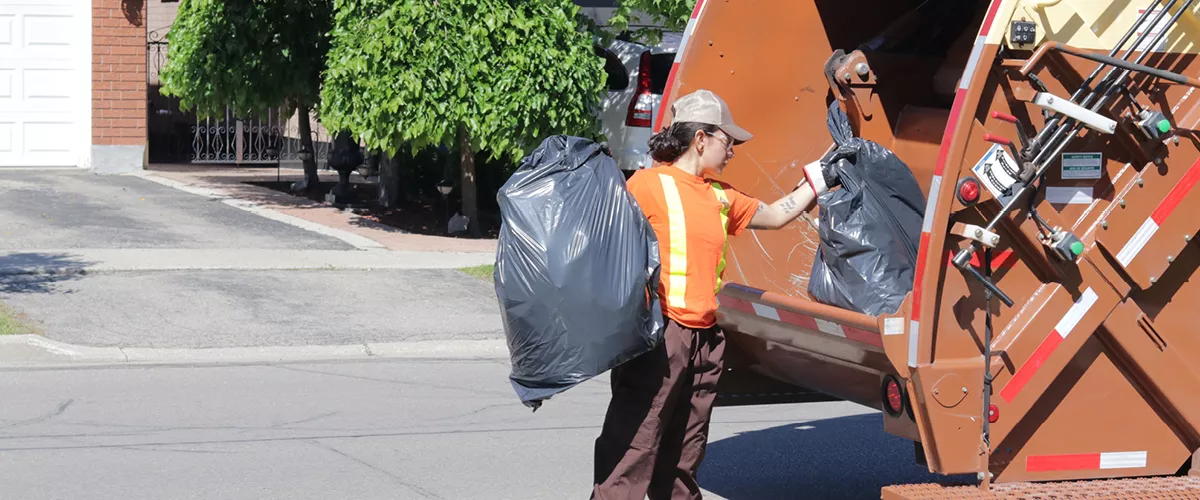 A person placing a bag of garbage in a garbage truck.