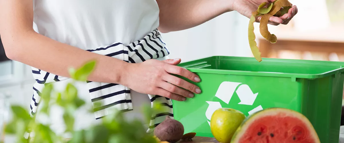 A person throwing food waste in a green bin.