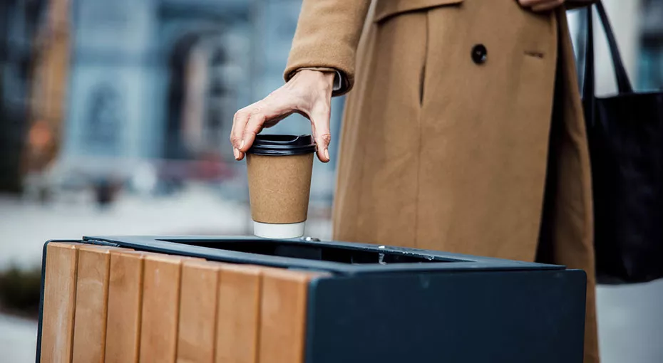 Image of a person throwing a coffee cup in the garbage