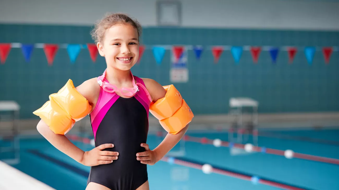 Girl standing next to indoor pool with water wings