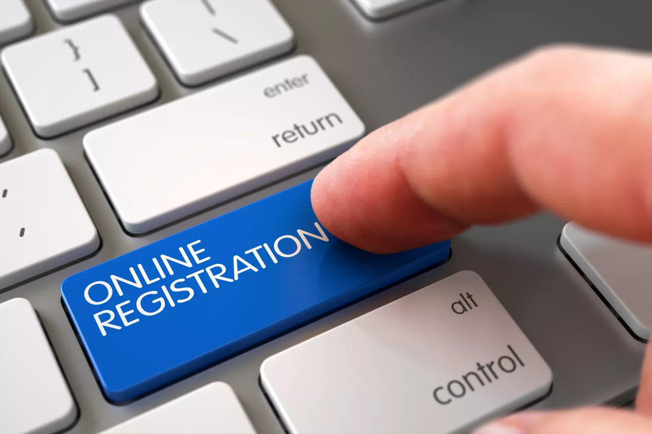 A finger pressing a blue button on a keyboard that says online registration 