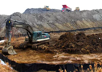Site undergoing alteration with an excavator piling soil and other machinery in the background.