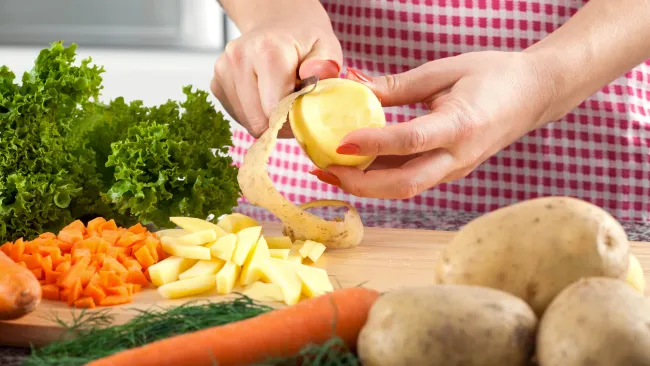 someone peeling a potato on a cutting board