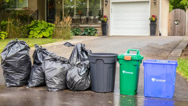 four garbage bags, one green bin and one blue box at the end of a driveway
