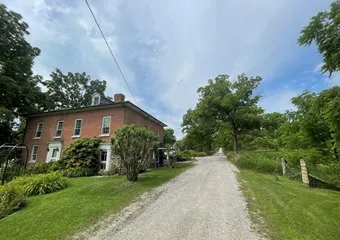 An image of a road with a house on the left side and trees lining the road.