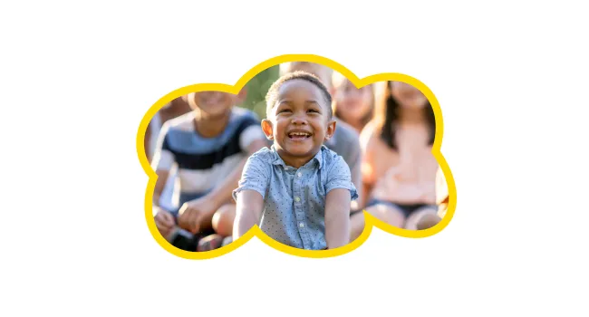 Dark skinned child smiling with his legs crossed, he is wearing a short sleeve blue shirt. The image is in the shape of a cloud.