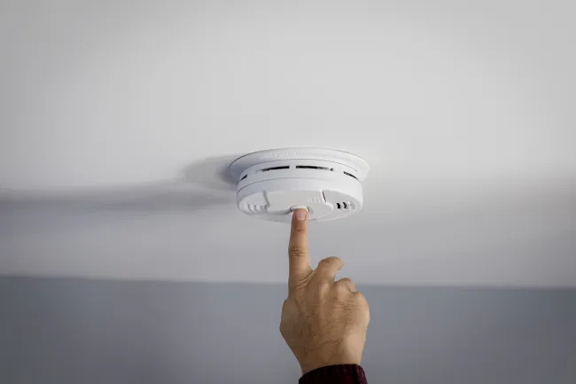 Finger pressing button on ceiling smoke detector