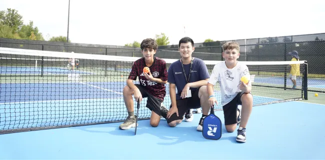A Vaughan pickleball instructor and two boys posing on the outdoor pickleball court at Carrville Community Centre