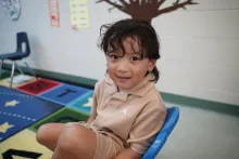Preschool boy wearing a beige shirt, sitting and smiling at the camera