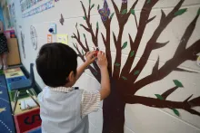 Preschool boy putting a apple illustration on a flat tree on the wall