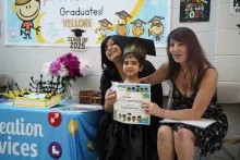 Preschool child with a graduation cap, smiling in the centre of two female teachers
