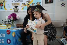 Preschool child with a graduation cap, smiling in the centre of two female teachers