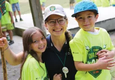 A camp counsellor and two attendees smiling.