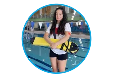 A female lifeguard standing in front of a pool holding a bright yellow rescue device.