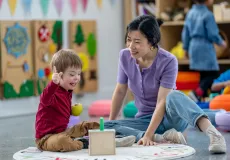 little boy playing in a classroom with a women helping him
