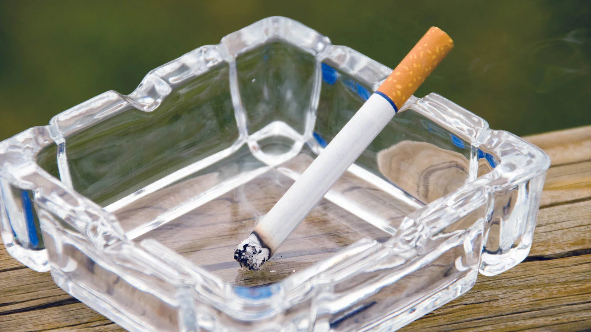 Lit cigarette in a glass ashtray
