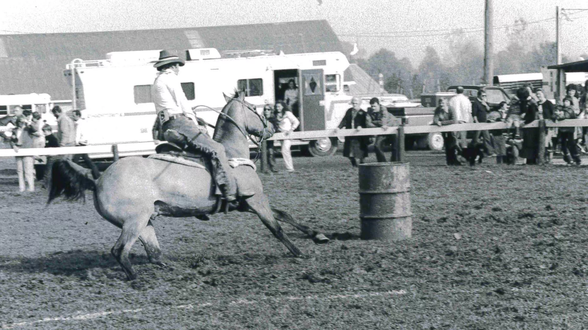 A man riding a horse around a barrel in a black and white photo