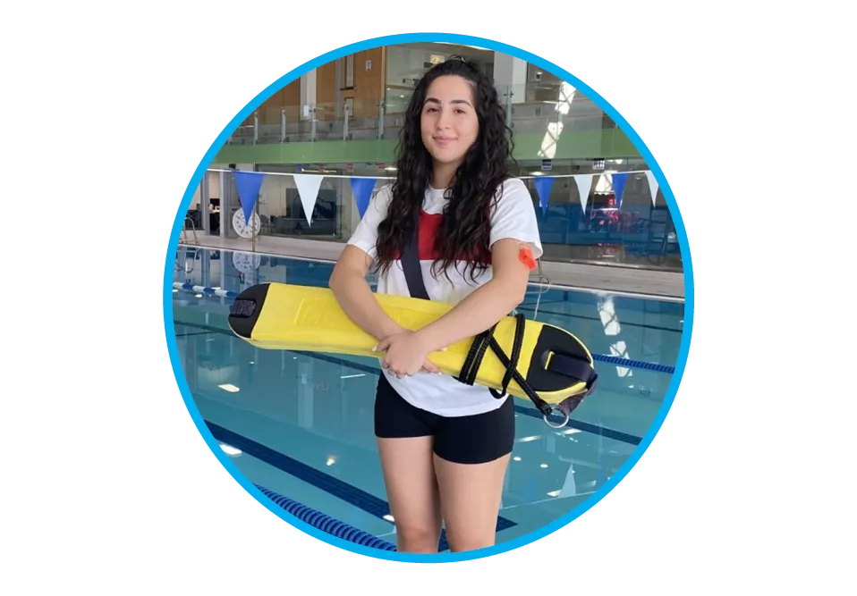 A female lifeguard standing in front of a pool holding a bright yellow rescue device.