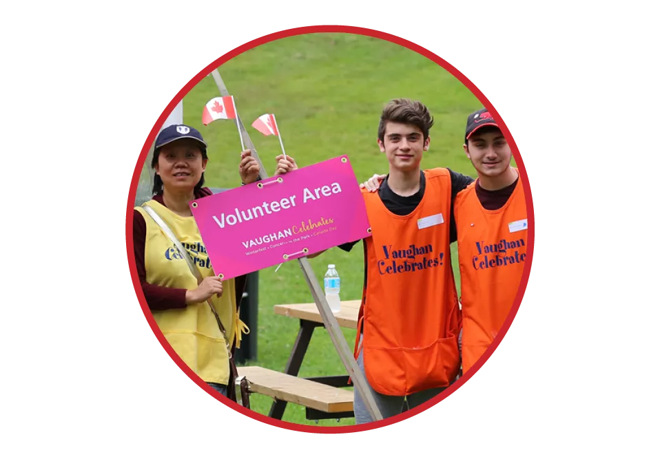 A group of three volunteers wearing bright orange or yellow vests holding a bright pink sign that says "Volunteer Area."