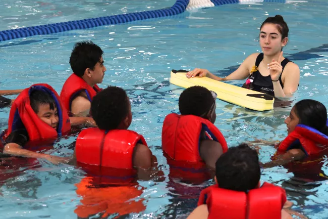 Instructor in pool teaching a swimmers with lifejackets on