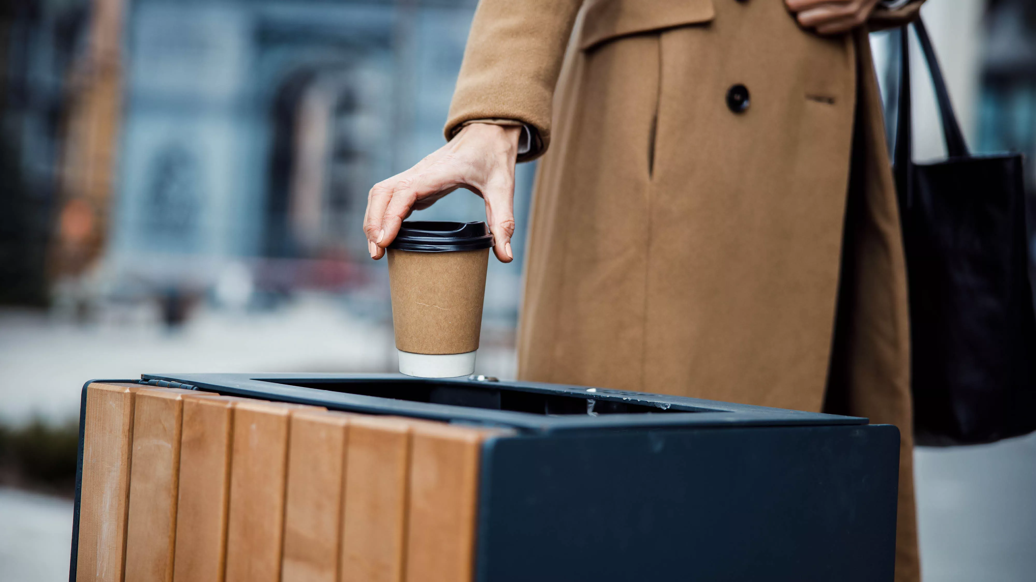 A person placing a coffee cup in the garbage bin